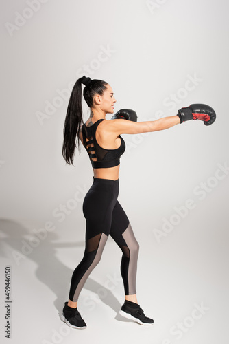 full length of happy sportswoman in boxing gloves working out on grey
