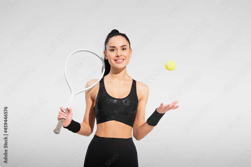 young sportswoman holding tennis racket and throwing ball on grey young sportswoman holding tennis racket and throwing ball on grey