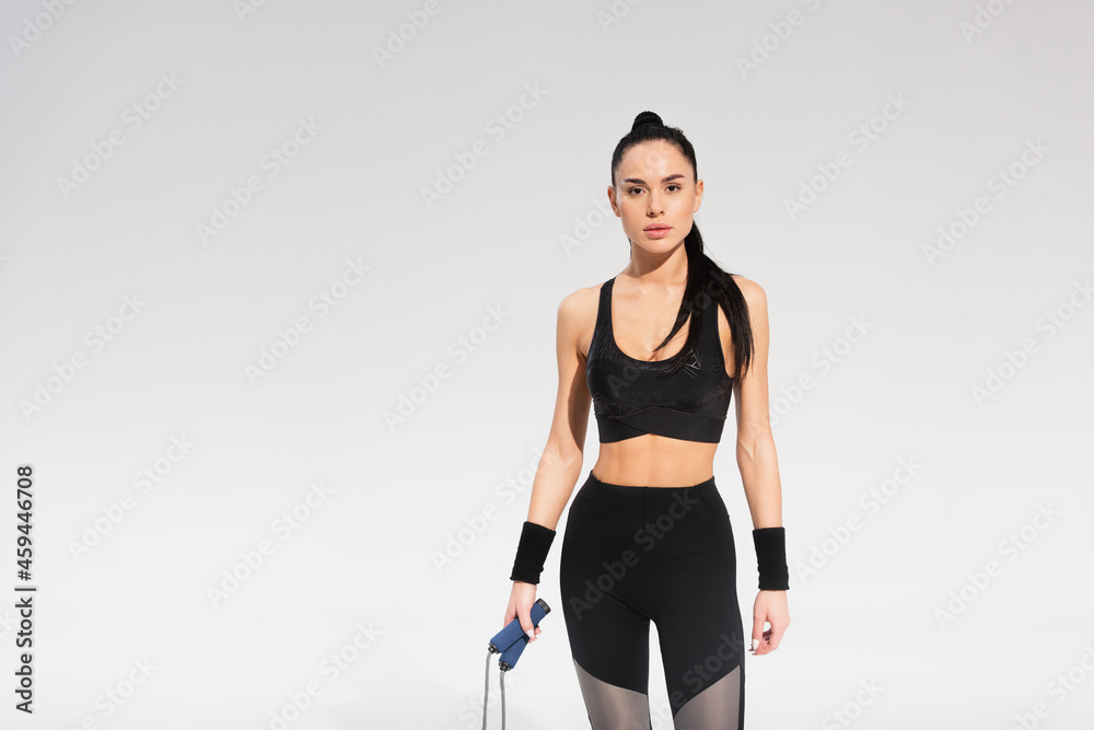 young sportswoman holding skipping rope on grey young sportswoman holding skipping rope on grey