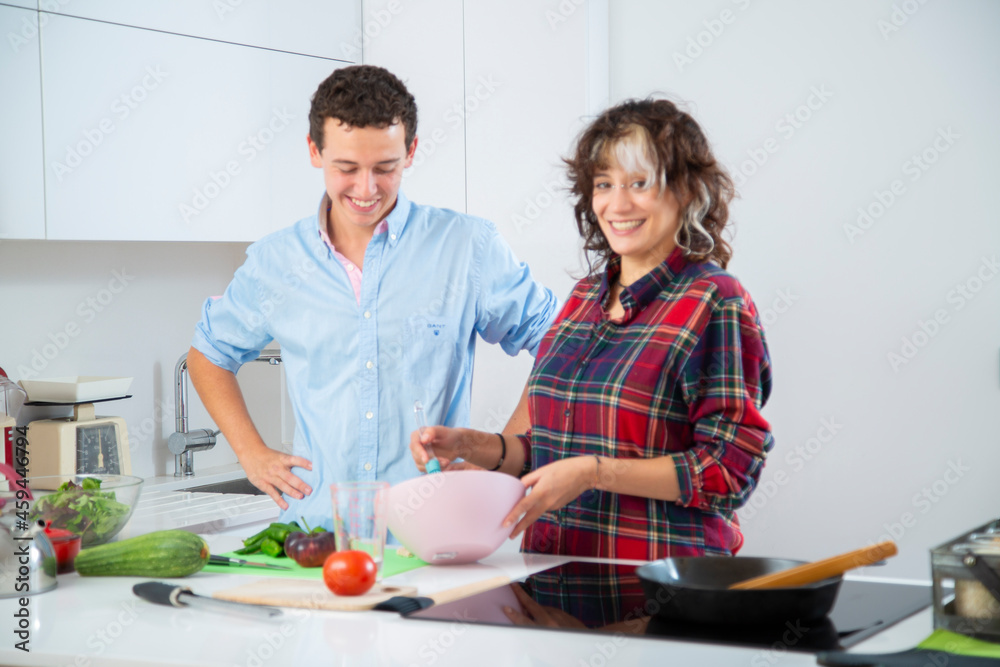 mujer joven sonriente bate huevos con su novio en cocina blanca de casa para cocinar un pastel mujer joven sonriente bate huevos con su novio en cocina blanca de casa para cocinar un pastel