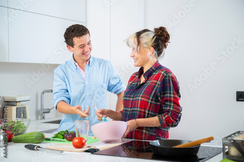 mujer joven sonriente bate huevos con su novio en cocina blanca de casa para cocinar un pastel 