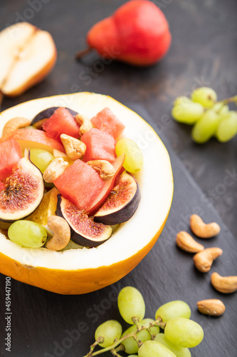 Vegetarian fruit salad of watermelon, grapes, figs, pear, orange, cashew  on black concrete background. Side view, selective focus.