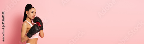 Bild auf Leinwand strong woman in sportswear and boxing gloves exercising on pink, banner