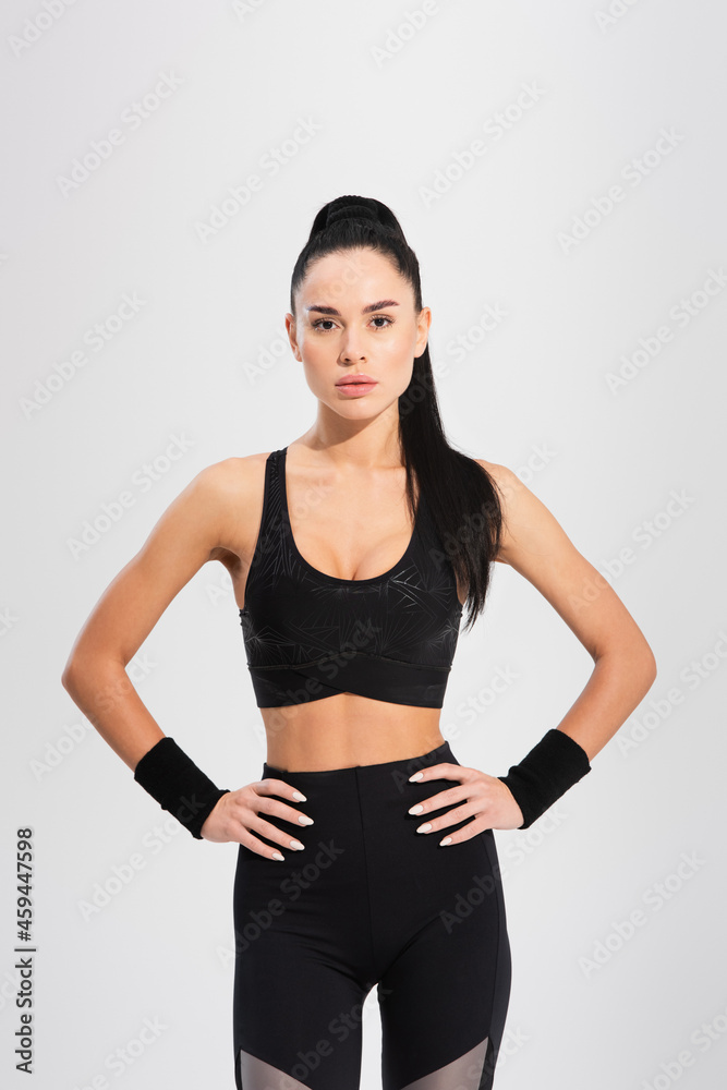 young confident sportswoman standing with hands on hips isolated on grey young confident sportswoman standing with hands on hips isolated on grey