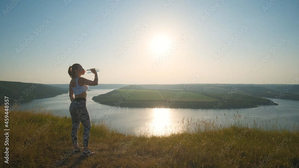 The sportive woman drinking water on a beautiful river background