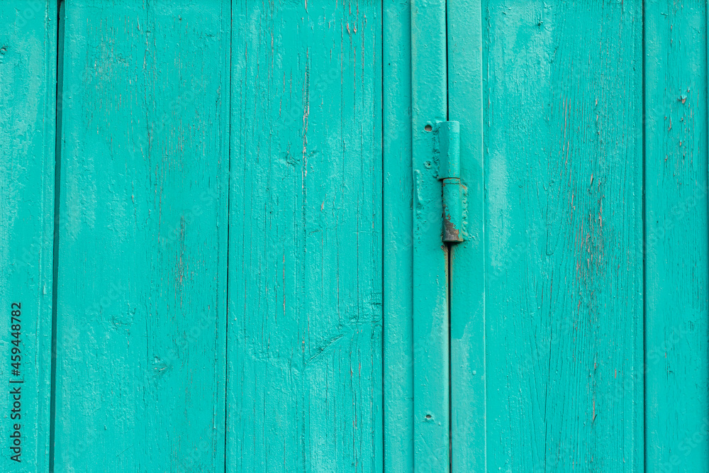 A fragment of an old wooden door of blue or turquoise color on rusty hinges.