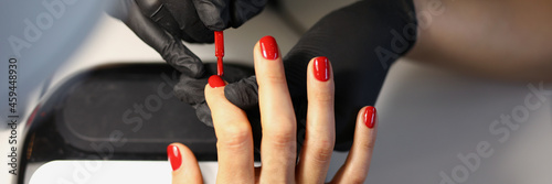 Master making red manicure to client in beauty salon closeup