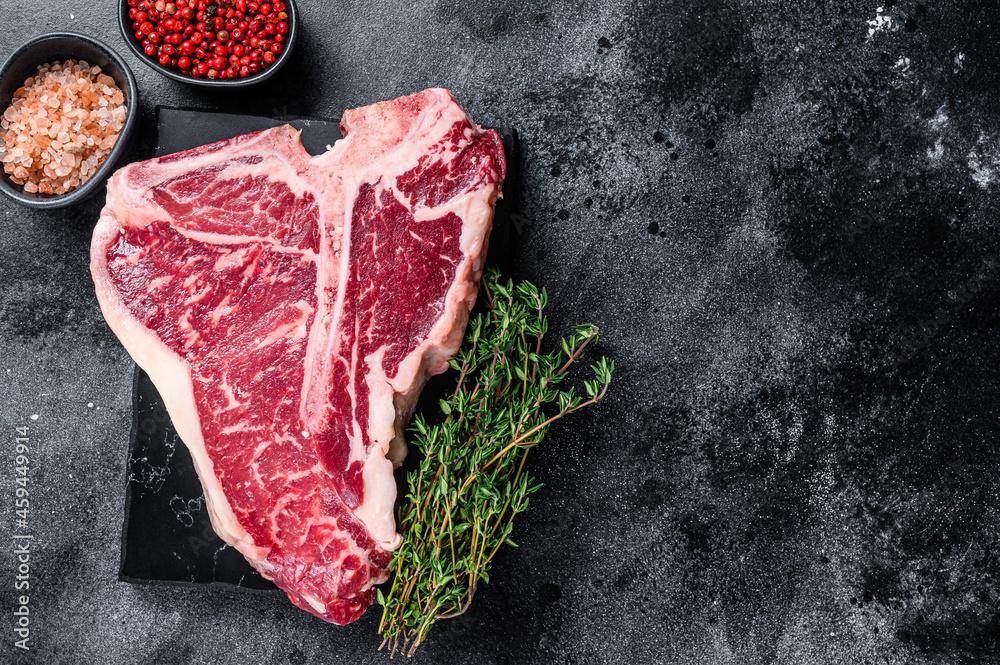 Dry-aged Raw T-bone or porterhouse beef meat Steak with herbs and salt. Black background. Top view. Copy space