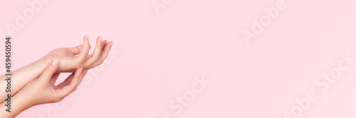 Female hands with beautiful manicure - pink nude nails on pink background  wide panoramic banner with copy space. Nail care concept