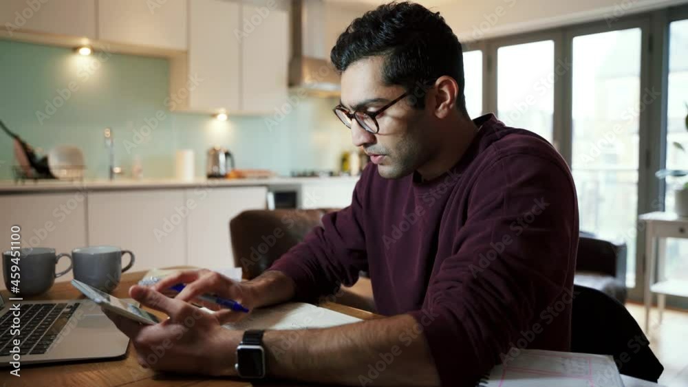Caucasian business man reading off digital tablet writing down notes sitting at desk Caucasian business man reading off digital tablet writing down notes sitting at desk