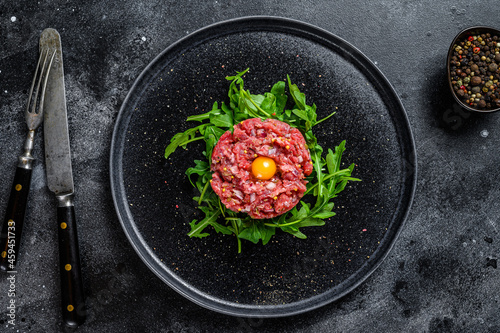 Beef tartare with arugula and quail egg. Black background. Top view photo