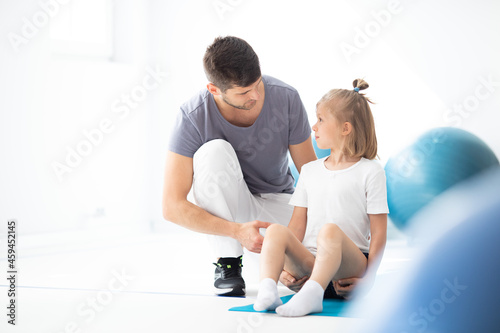 Cute school girl sitting on blue yoga mat talking to her handsome young physician