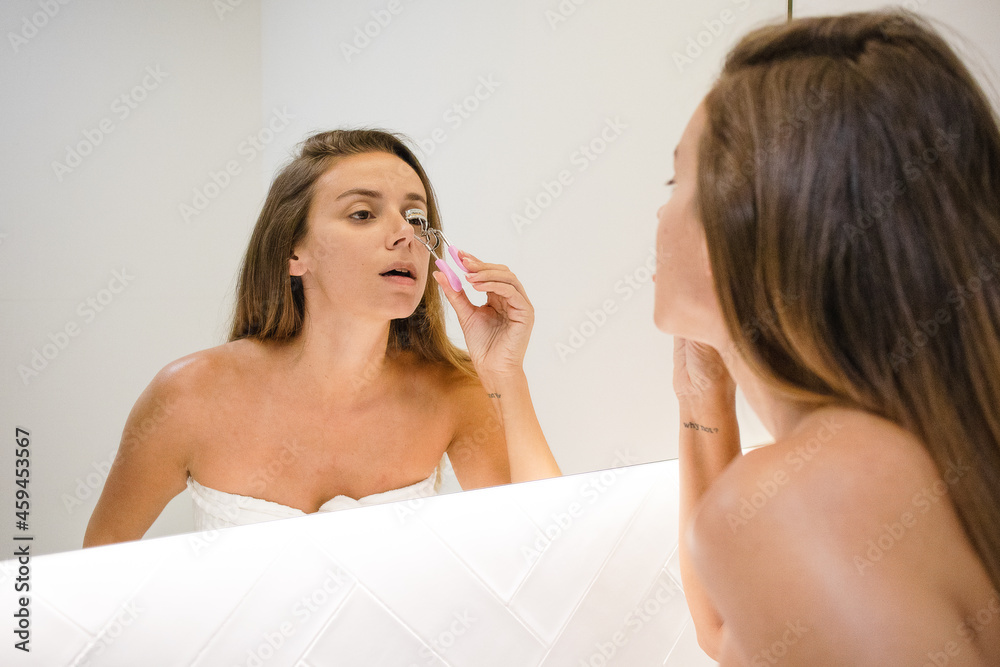 young woman using eyelash curler at home no makeup long hair after shower looking at herself in the bathroom mirror doing self care makeup routine refreshed confident getting ready to go out lash curl young woman using eyelash curler at home no makeup long hair after shower looking at herself in the bathroom mirror doing self care makeup routine refreshed confident getting ready to go out lash curl