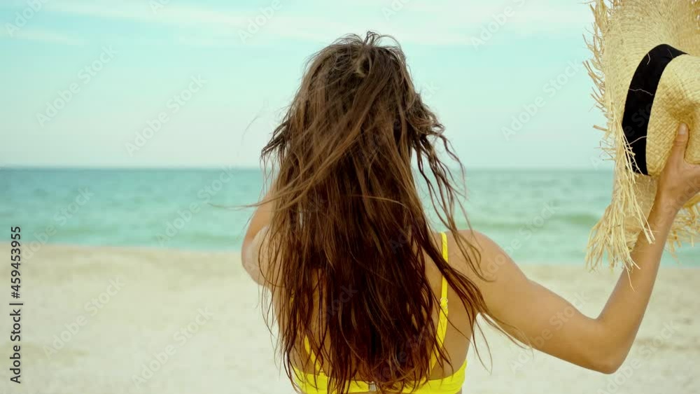 rear view beach body woman in yellow bikini with straw hat walking on beach to sea, healthy girl with firm buttocks rear view beach body woman in yellow bikini with straw hat walking on beach to sea, healthy girl with firm buttocks