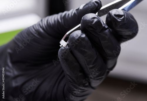 Close up of orthodontist in black sterile glove holding stainless steel instrument with orthodontic bracket. Dental tools for attaching braces to teeth. Concept of dentistry and orthodontic treatment.