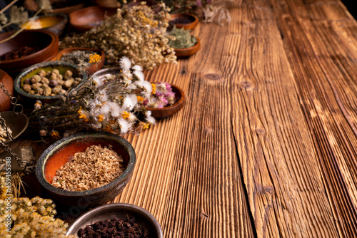 Natural medicine background. Assorted dry herbs in bowls and brass mortar on rustic wooden table.