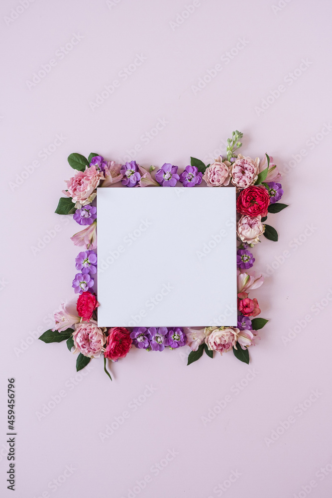 Frame made of rose flower buds on pink background and blank paper card sheet. Flat lay, top view. Copy space mockup.