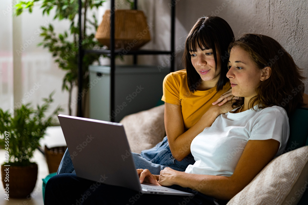 Lesbian couple using laptop while sitting on sofa at home Lesbian couple using laptop while sitting on sofa at home