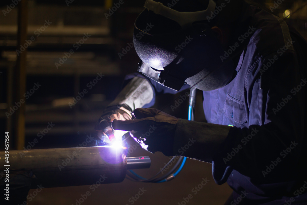 Skillful welders weld steel in the factory. Construction site metal welder. builder wear fireproof gloves for safety at work.