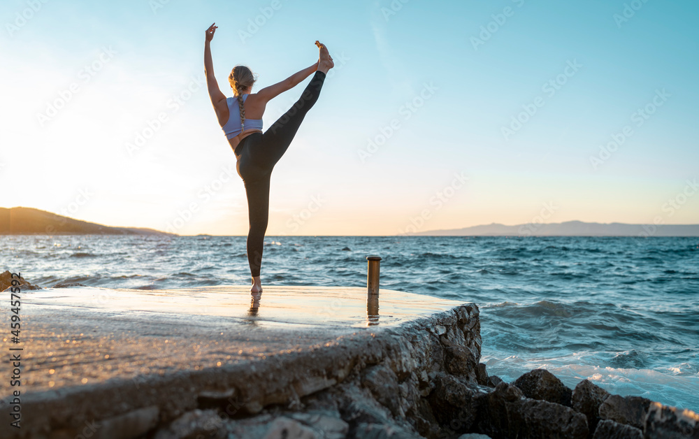 junge Sportlerin macht eine sehr anspruchsvolle Yoga Figur und greift mit der ausgestreckten Hand an den gestreckten Fuß