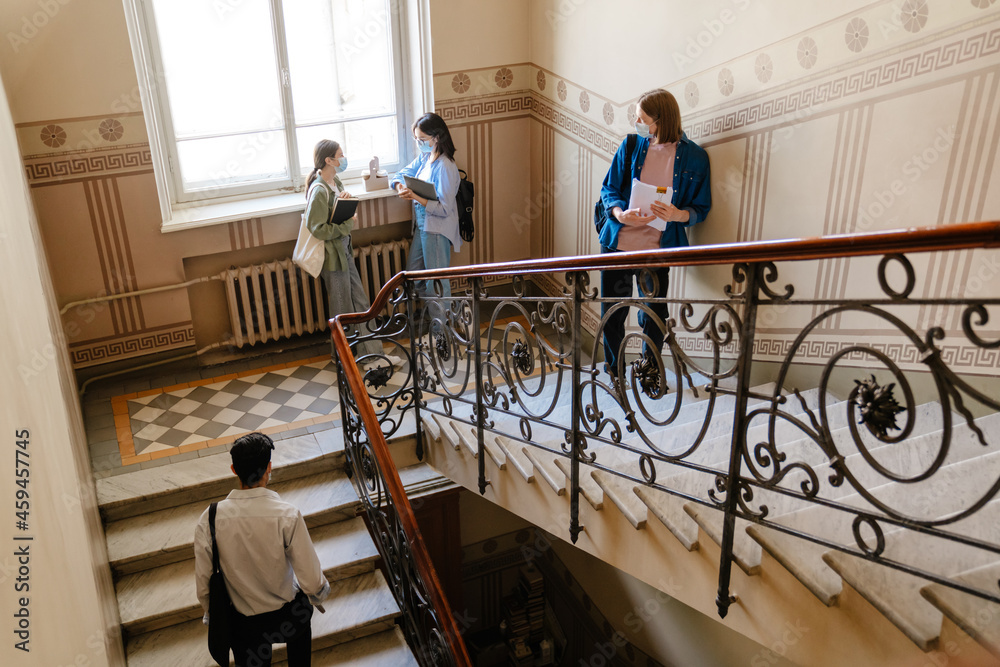 Young students in face mask standing and talking on university stairs Young students in face mask standing and talking on university stairs