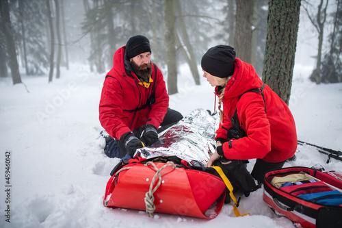 Mountain rescue service provide operation outdoors in winter in forest, injured person in stretcher.