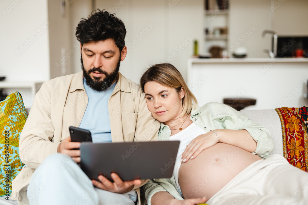 Bearded man and pregnant woman using gadgets while sitting on couch Bearded man and pregnant woman using gadgets while sitting on couch