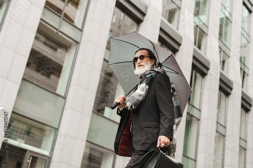 White senior man walking under umbrella at city street