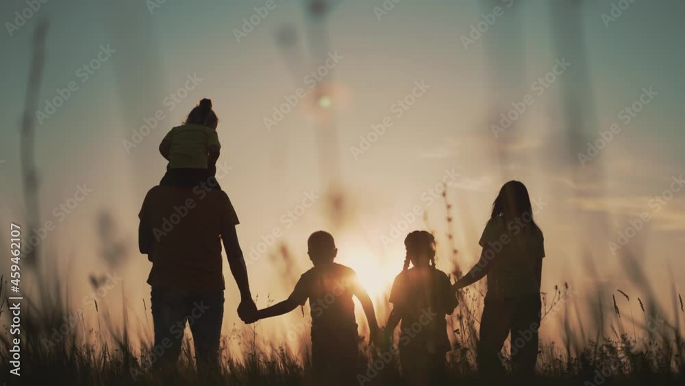 Happy family at sunset. Silhouette of group of people walk in park. Happy child with parents holding hand. Family is walk in park on grass. Happy family concept. Parents hold hand of their child.