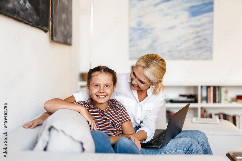 White mother and daughter smiling and using cellphone at home White mother and daughter smiling and using cellphone at home
