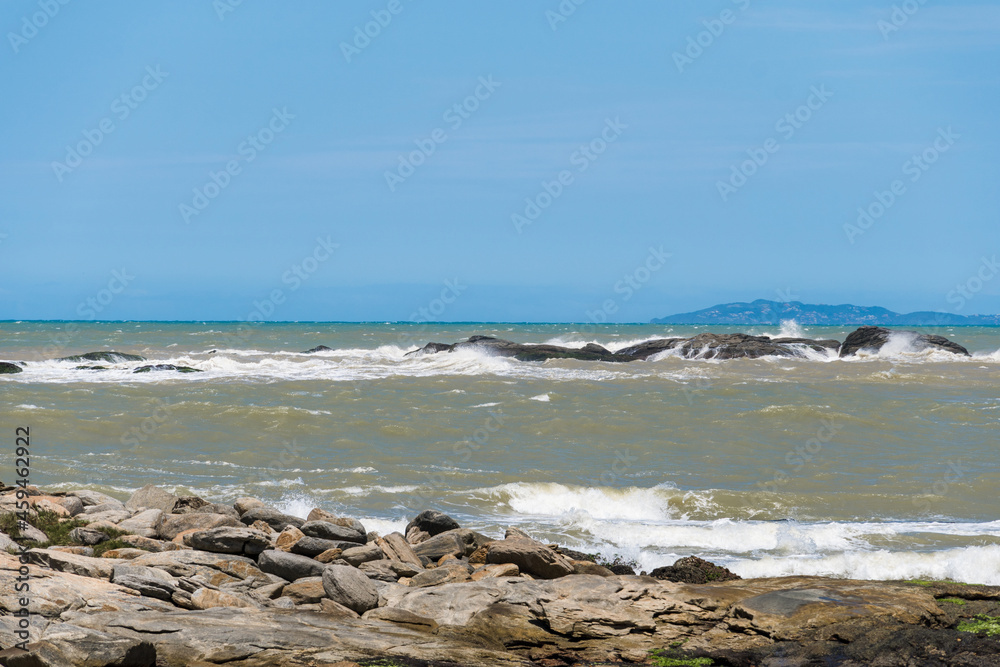 View of the Joana beach in Rio das Ostras in Rio de Janeiro. Sunny day, blue sky. Strong sea and yellowish sand and lots of rocks. View of the Joana beach in Rio das Ostras in Rio de Janeiro. Sunny day, blue sky. Strong sea and yellowish sand and lots of rocks.