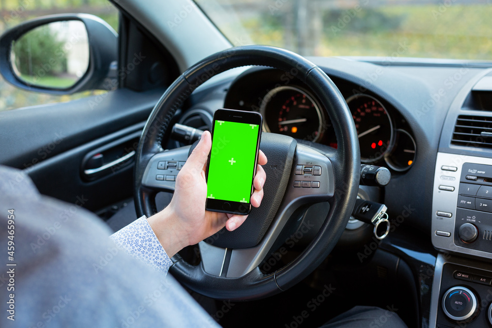 Mobile phone with green screen in car background.