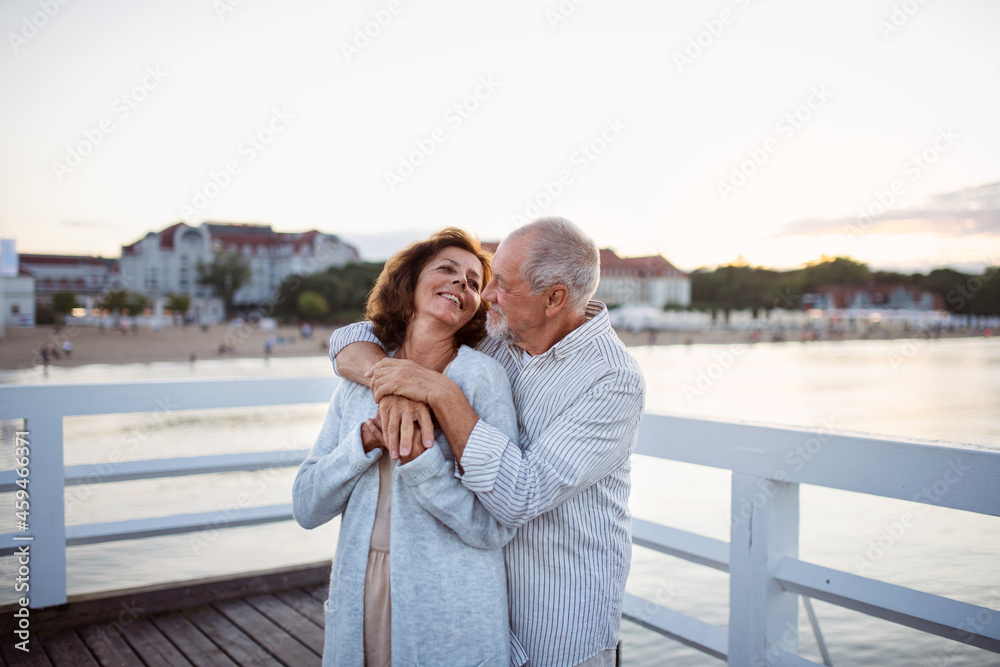 Happy senior couple hugging outdoors on pier by sea, looking at each other.