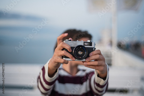 Close up of girl taking photo with camera on pier by sea at sunset, holiday concept.