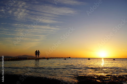Colorful sunset by the ocean, two people walk across the bridge, two silhouettes             
