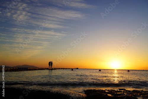 Colorful sunset by the ocean, two people walk across the bridge, two silhouettes             
