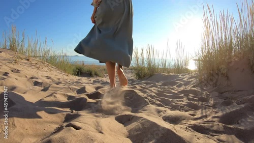 Close-up of the slender legs of a young woman walking along a deserted northern beach among the sand dunes in the rays of the setting rising sun. Yyteri beach, Finland