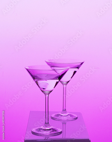 Two martini glasses transparent agains colorful background yellow red blue green 
