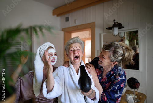 Happy senior women friends in bathrobes having fun indoors at home, selfcare concept. photo