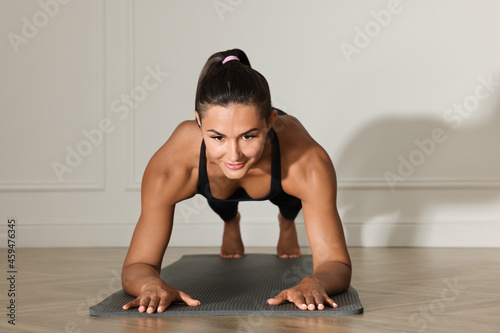 Young woman doing plank exercise near white wall © New Africa