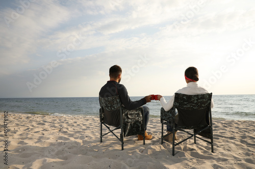 Couple sitting in camping chairs and clinking mugs on beach, back view © New Africa