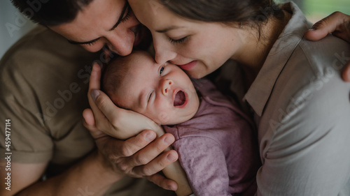 Close up of young parents holding and kissing their newborn baby indoors at home photo
