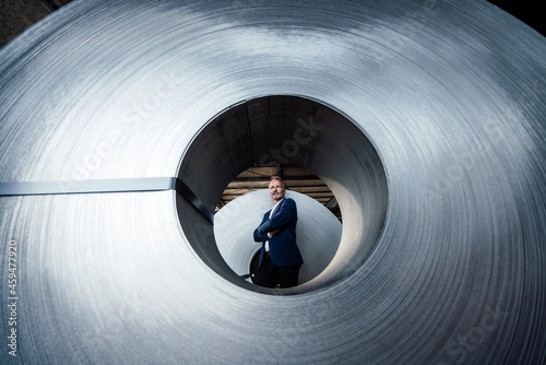 Confident male business professional standing with arms crossed in steel mill photo