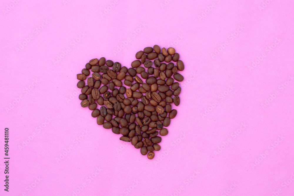 The coffee beans are laid in the shape of a heart. Greeting card design on a pink background The coffee beans are laid in the shape of a heart. Greeting card design on a pink background