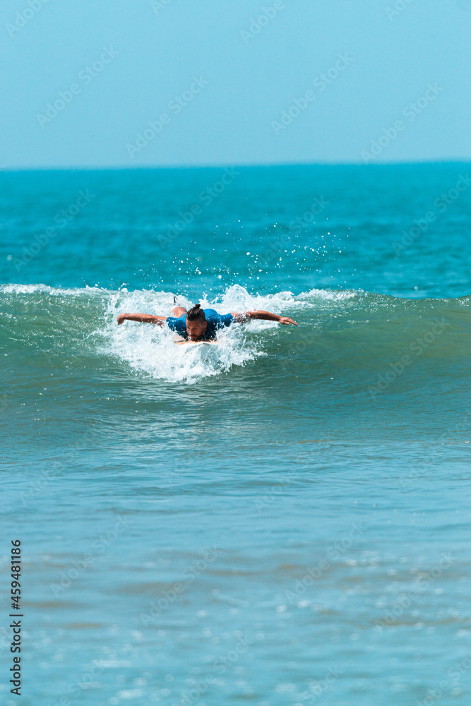 Surfer mężczyzna łapiący falę na desce na tle niebieskiego oceanu i błękitnego nieba. - obrazy, fototapety, plakaty 