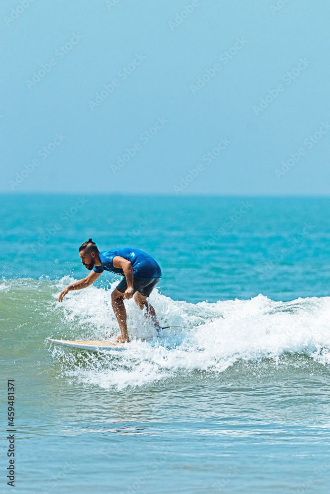 Naklejka premium Mężczyzna surfer płynący na fali na tle błękitnego oceanu i nieba.