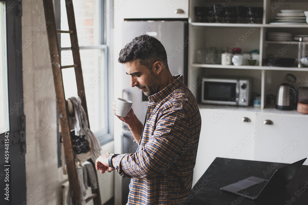 Hispanic mid adult male having morning coffee and looking at smartwatch Hispanic mid adult male having morning coffee and looking at smartwatch