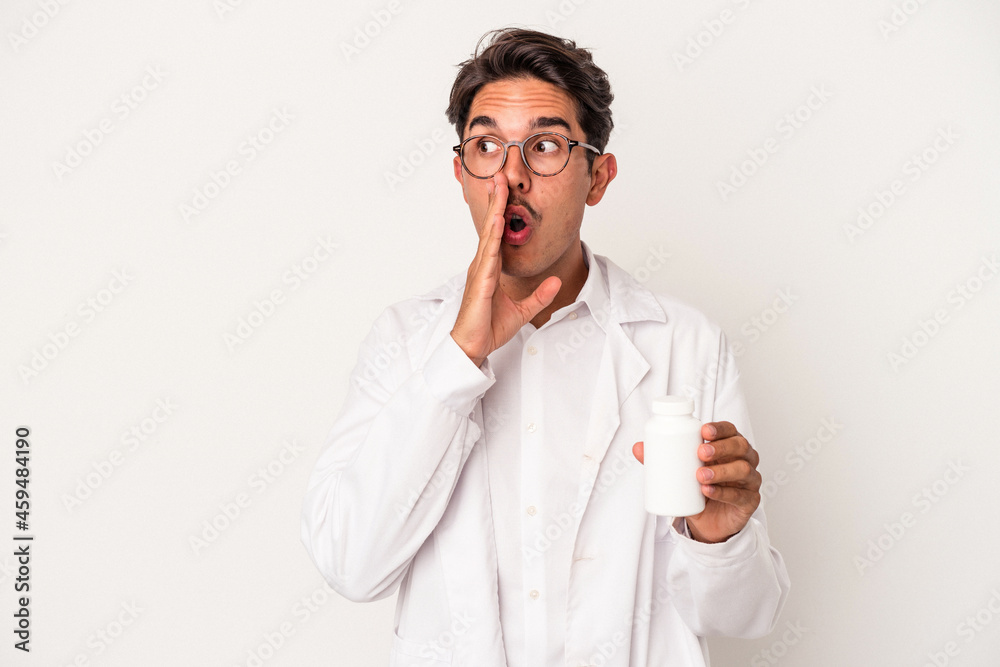 Young pharmacist mixed race man holding pills isolated on white background is saying a secret hot braking news and looking aside Young pharmacist mixed race man holding pills isolated on white background is saying a secret hot braking news and looking aside