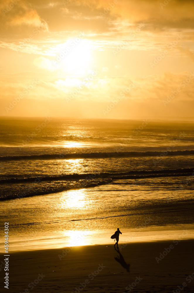 A silhueta de um surfista e sua prancha saindo do mar durante o pôr do sol. 