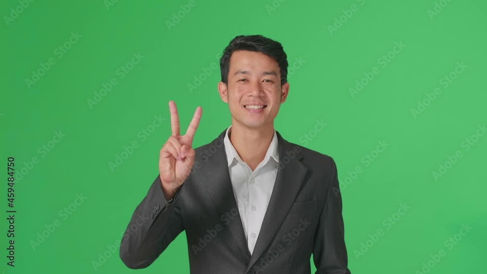 A Smiling Young Asian Business Man Showing Gesture Peace While Standing On Green Screen In The Studio
A Smiling Young Asian Business Man Showing Gesture Peace While Standing On Green Screen In The Studio